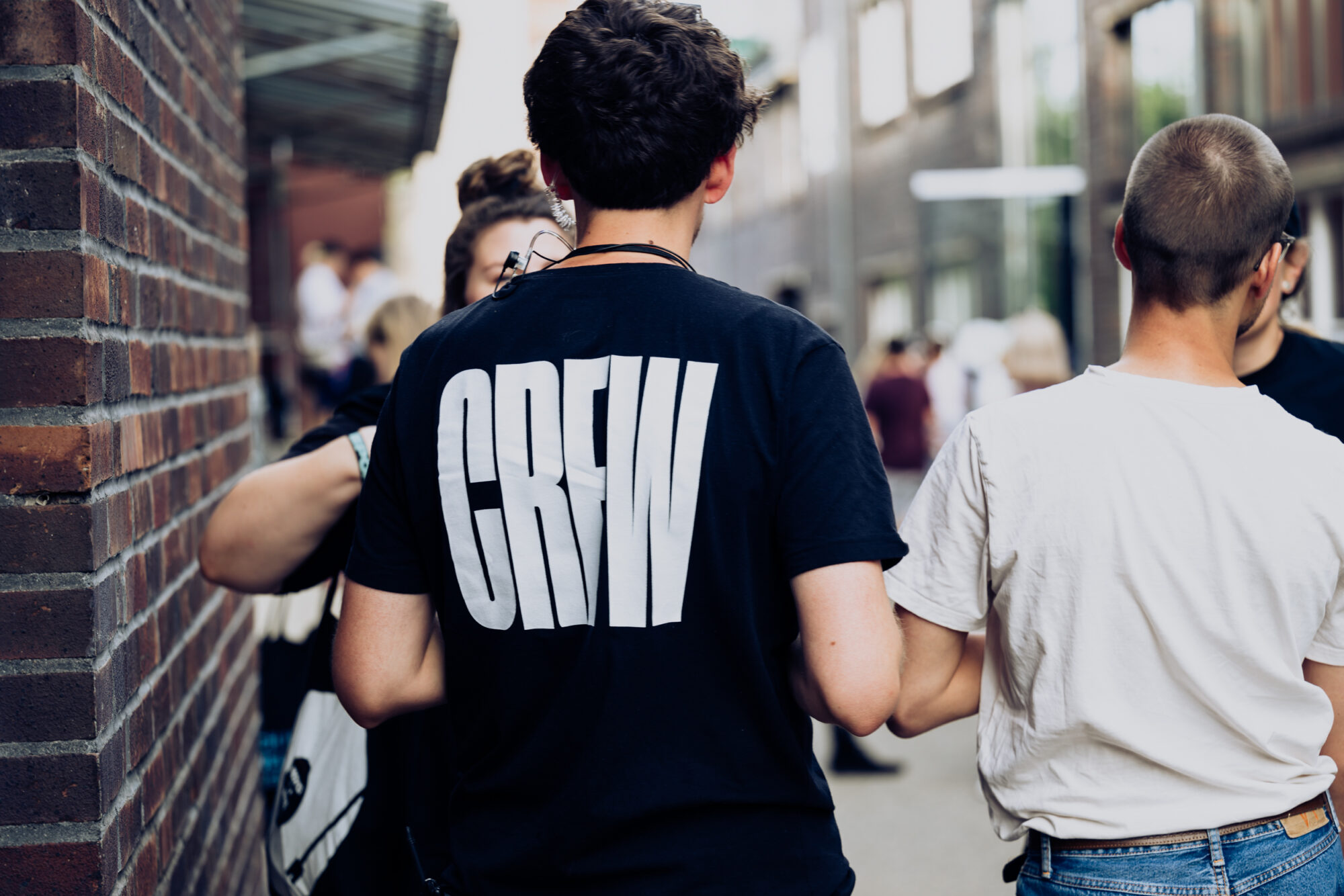 Eine Gruppe Menschen mit dem Rücken zur Kamera. Auf dem Tshirt der linken Person steht groß Crew