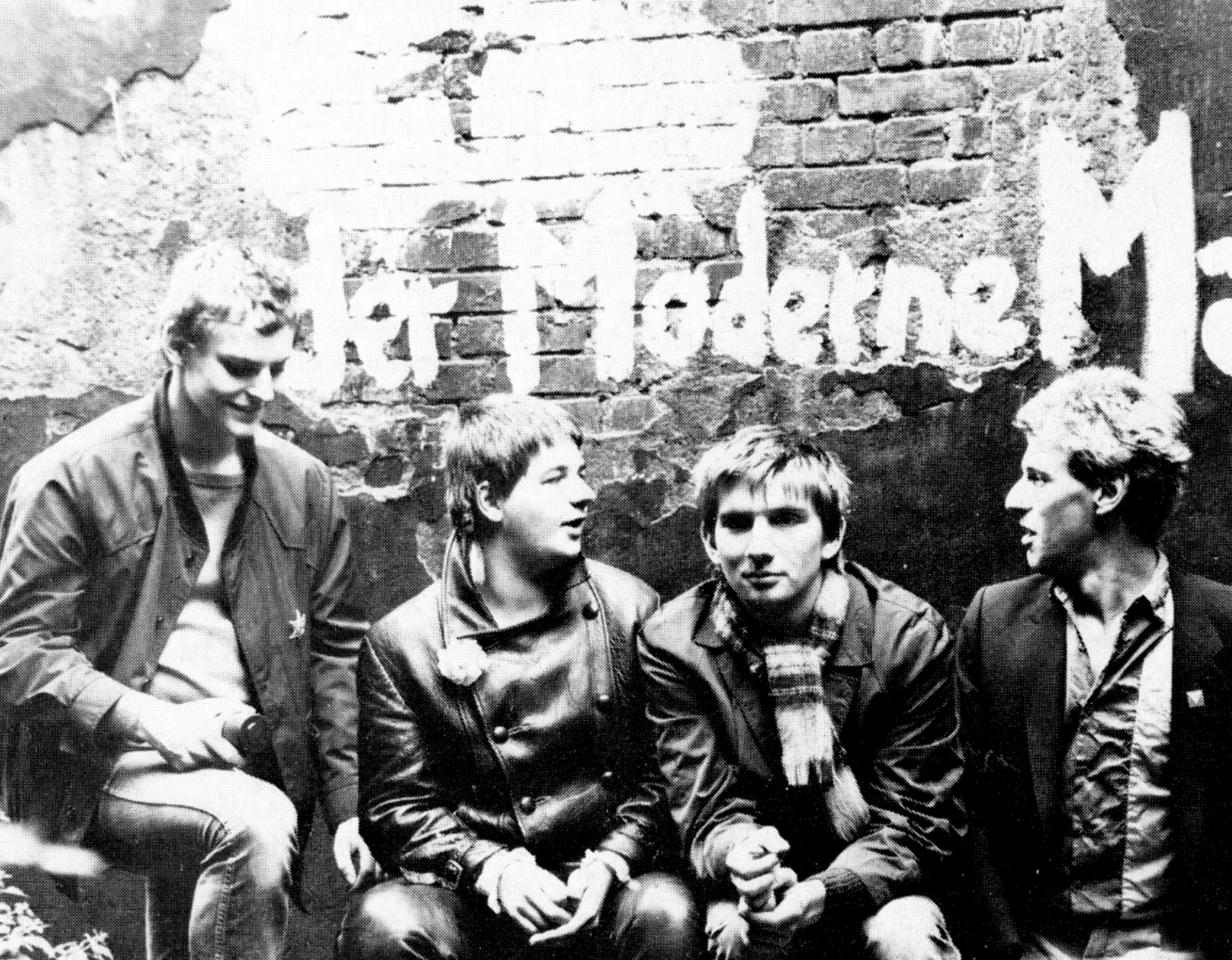 Ein altes schwarz-weiß Bild von vier Männern, die vor einer Wand knien.