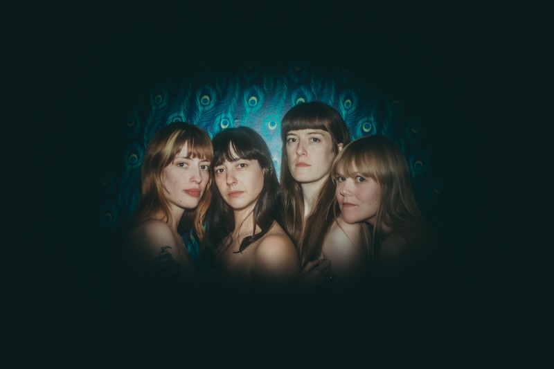 Das Bild von Los Bitchos zeigt die vier Bandmitgliederinnen. Sie stehen nah beieinander, nur ihre Gesichter, die alle von mittellangem Haar und einem kurzen Pony eingerahmt sind sind zu sehen. Sie blicken alle in die Kamera.